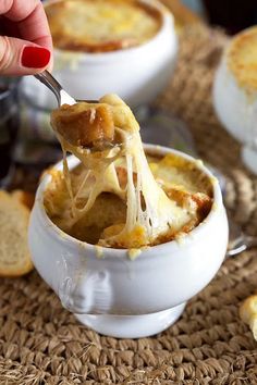 a person is spooning some food out of a white bowl with bread on the side