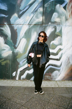 a woman standing in front of a graffiti wall with her hands in her pockets and wearing sunglasses