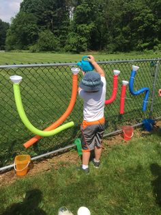 a little boy is playing with some water hoses on the side of a fence