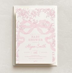 a pink and white baby shower card with bows on it's front, sitting on top of a table