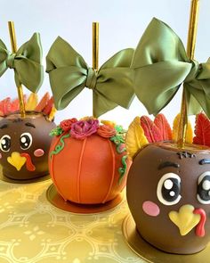 three chocolate covered apples decorated with bows and pumpkins on a yellow tableclothed surface