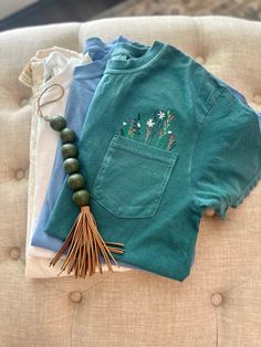 Calling all wildflower chicks!!  these beautiful embroidered Comfort Colors tees will brighten your day and cultivate kindness anywhere you go! Available in an array of color options, the recipient or yourself, will love this soft tee! Embroidery in a wildflower design is placed above the pocket as shown.  (Tee shown is emerald) **If you would prefer pocket monogramming, please see our listing here:  https://www.etsy.com/listing/1567262659/custom-comfort-colors-pocket-tee If you have any questio Spring Cotton Tops With Floral Embroidery, Spring Floral Embroidered Cotton Tops, Green Cotton Top With Floral Embroidery, Cotton Tops With Floral Embroidery For Spring, Casual Multicolor Embroidered T-shirt For Spring, Casual Spring Embroidered T-shirt, Spring Casual T-shirt With Floral Applique, Blue Floral Embroidery Short Sleeve T-shirt, Blue Floral Embroidered Short Sleeve T-shirt