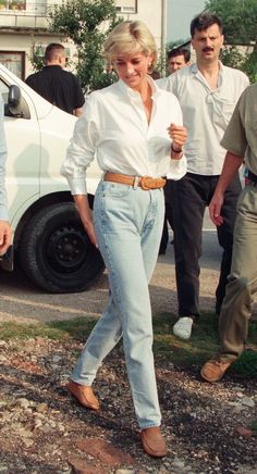 a woman in white shirt and jeans walking on the street with other people behind her