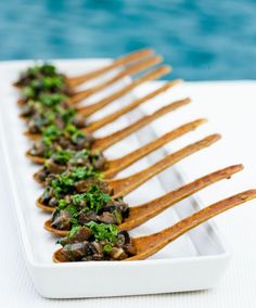 several forks are lined up on a white plate next to the water, with mushrooms and parsley in between them