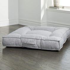 a gray dog bed sitting on top of a hard wood floor next to a window