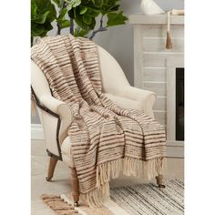 a chair with a blanket on it in front of a fire place and potted plant