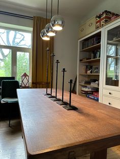 a large wooden table with four lights hanging from it's center and two chairs in the background