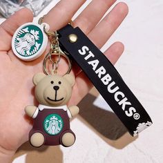 a hand holding a starbucks keychain with a teddy bear on it's chest