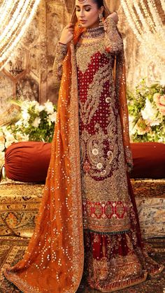 Mesmerising red hued long shirt crafted with heavy hand worked details on front and back, paired with embellished gharara and a stunning orange rust muskesh worked dupatta. Pakistani Bridal Couture, Pakistani Bridal Dress, Indian Wedding Gowns, Walima Dress, Red Bridal Dress