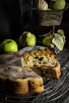 a cake on a wire rack next to some apples and other fruit in the background