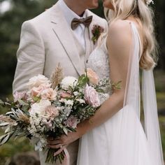 a bride and groom kissing each other in front of some trees with their bouquets