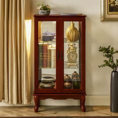 a wooden cabinet with glass doors in front of a window next to a potted plant