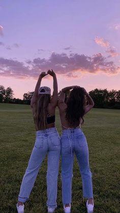 two women standing in the grass with their arms around each other as they look up into the sky