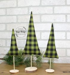 three green and black plaid christmas trees sitting on top of a wooden table