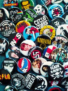 many different colored and black buttons on a blue cloth with the names of famous rock bands