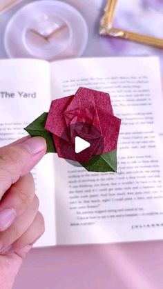 a person is holding an origami rose in front of a book with the pages open