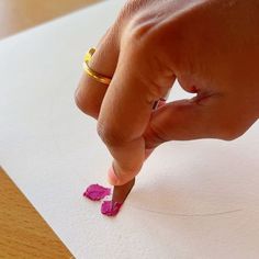 a person is writing on paper with a pencil and some pink crayons in front of them