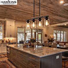 a large kitchen island with lights hanging from it's ceiling and chairs around it