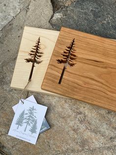 two wooden cutting boards with trees cut out of them sitting on top of some rocks