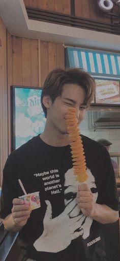 a young man holding up a piece of food in front of his face while standing next to a fast food stand