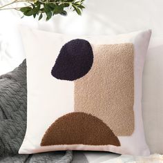 a decorative pillow on a couch with a plant in the back ground and white walls behind it