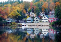 houses on the shore of a lake surrounded by trees with fall foliage in the background