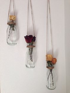 three glass vases with flowers hanging from the side, one holding dried roses and two without