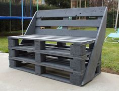 a bench made out of pallets sitting on top of a cement slab in front of a playground