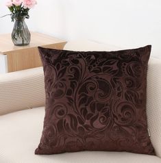 a brown pillow sitting on top of a white couch next to a vase with flowers