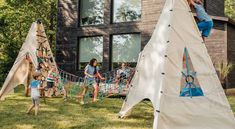 two teepee houses with kids playing in the yard and one has a slide on it