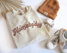 Homebody's unite Live your best lounge life in this cozy crew neck sweatshirt. It is sure to keep you feeling all warm and fuzzy all season long. Beige Letter Print Sweatshirt For Loungewear, Trendy Cream Sweatshirt For Loungewear, Cream Letter Print Sweatshirt For Loungewear, Trendy Cream Sweatshirt, Cute Sweatshirt Designs, Homebody Shirt, Beige Sweatshirt, Market Ideas, Summer Graphic Tee