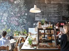 people sitting at tables in front of a chalkboard wall with floral designs on it