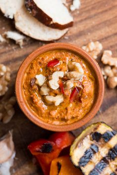 a wooden table topped with a bowl of hummus next to grilled vegetables and bread