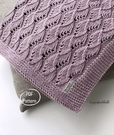 a purple knitted blanket sitting on top of a pillow next to a gray pillow