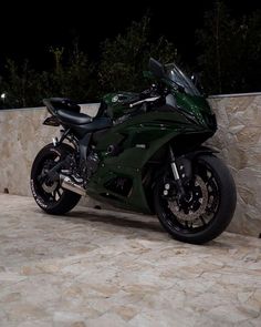 a dark green motorcycle parked next to a stone wall at night with its lights on