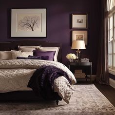 a large bed sitting in a bedroom next to a window covered in purple and white pillows