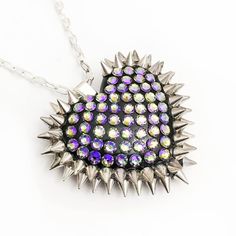 Featuring a stunning heart-shaped pavé pattern adorned with dozens of sparkling crystals and spikes, this necklace is perfect for layering or wearing alone. Its "mini" size makes it versatile and easy to wear, while still delivering the same high-impact statement as the classic version. Paradise boasts a stunning combination of deep sea blue and golden sunlight hues. The metallic pale gold shimmer on the surface adds a touch of glamour to this tropical-inspired colorway. It's like wearing a piec Heart-shaped Rhinestone Necklaces For Party, Heart Shaped Rhinestone Party Necklace, Party Heart Pendant Necklace With Rhinestones, Heart Pendant Rhinestone Necklace For Party, Heart Pendant Necklace With Bling For Party, Edgy Heart Pendant Necklace For Gift, Edgy Heart Pendant Necklace As Gift, Trendy Heart Shaped Rhinestone Jewelry, Trendy Spiked Jewelry For Parties