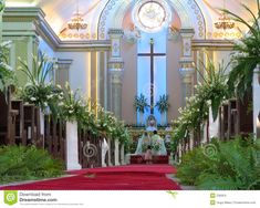 a person sitting on a red carpet in front of a cross and palm trees at the end of a church aisle