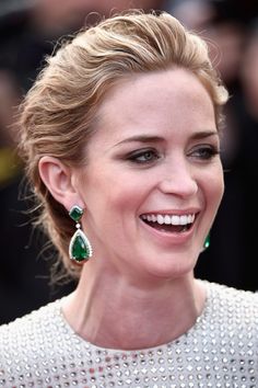 a woman smiling and wearing green earrings on her head at the red carpet for the oscars