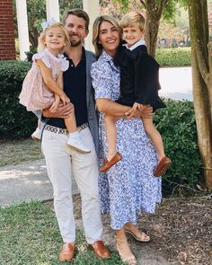 a man, woman and two children are standing in front of a house with trees