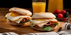 two sandwiches with eggs, ham and cheese on them sitting on a wooden cutting board