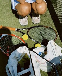 a woman sitting on the ground with her tennis racket and ball in front of her