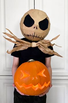 a young boy holding a pumpkin in front of his face and wearing a skeleton mask