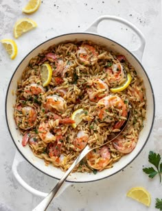 a skillet filled with pasta and shrimp, garnished with lemon wedges