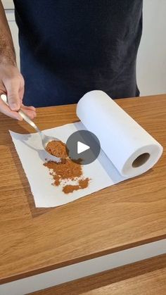 a person cutting up some food on top of a wooden table next to a roll of paper