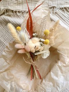 a bouquet of flowers is laying on a bed sheet with white and yellow feathers around it