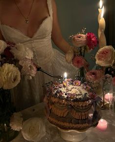 a woman in a wedding dress is cutting a cake with candles on the table next to her