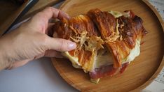 a person is holding up a sandwich on a wooden platter with bacon and cheese