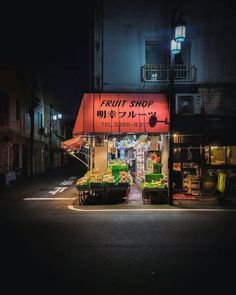 a fruit shop is lit up at night on the side of an empty city street