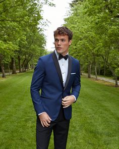 a man in a tuxedo poses for the camera while standing on some grass